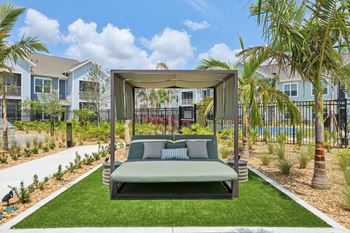 A green outdoor daybed with a canopy is situated in a landscaped yard.